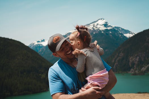 Tender moment of a father and daughter hugging in a scenic mountain setting.