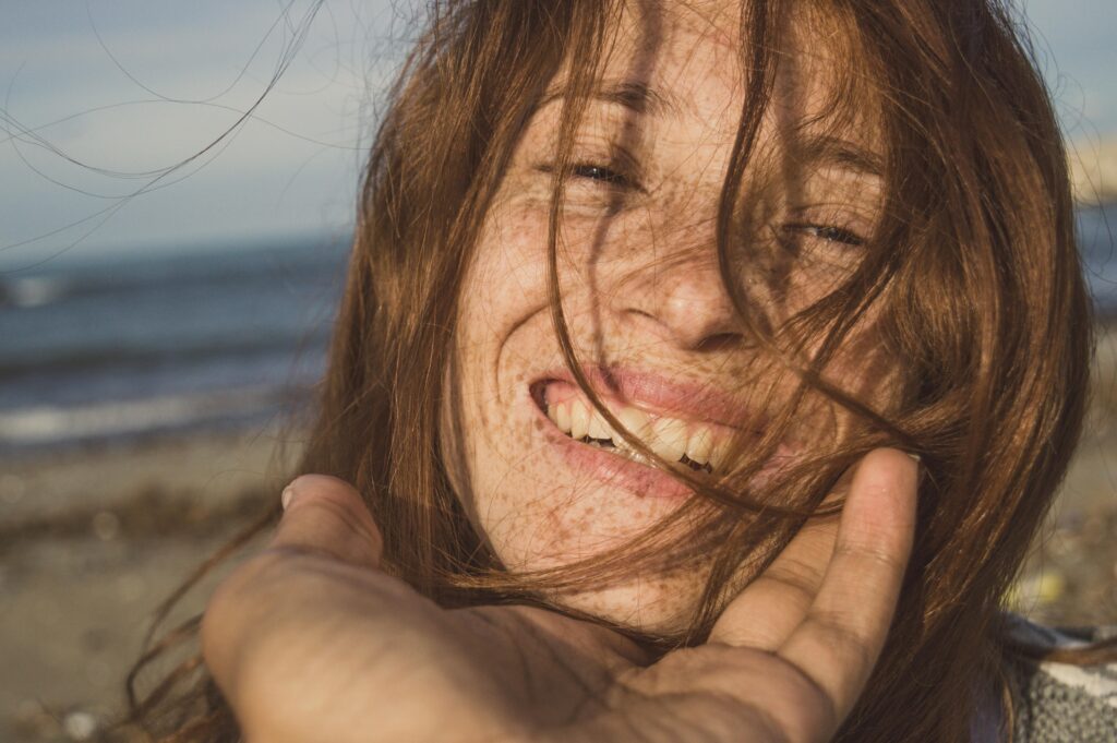 Close-up portrait of a smiling redhead woman on a beach, embracing her natural beauty.