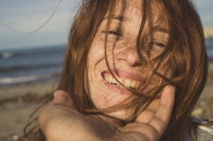 Close-up portrait of a smiling redhead woman on a beach, embracing her natural beauty.