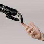 A human hand with tattoos reaching out to a robotic hand on a white background.