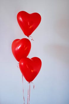 Three red heart-shaped balloons floating in a minimalist studio setting, evoking love and romance.